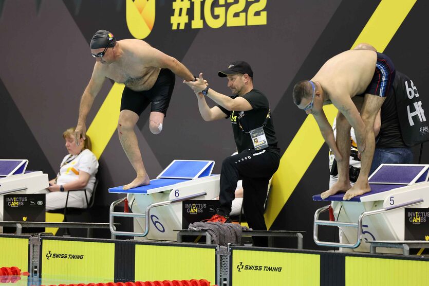 Ein beinamputierter belgischer Sportler nutzt auf dem Startblock beim Schwimmen den Haltegriff eines Teammitglieds während der Invictus Games 2022 in Den Haag/Niederlande.