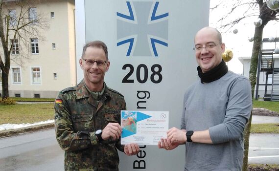 Oberstabsfeldwebel Thomas Stegmann (li.) übergibt dem sichtlich erfreuten Oberstabsgefreiten Eric Pszolla den Reisegutschein des BwSW.